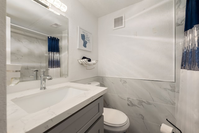 bathroom with toilet, visible vents, tile walls, and vanity