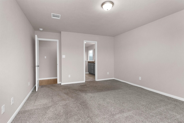 unfurnished bedroom featuring carpet floors, baseboards, visible vents, and ensuite bathroom