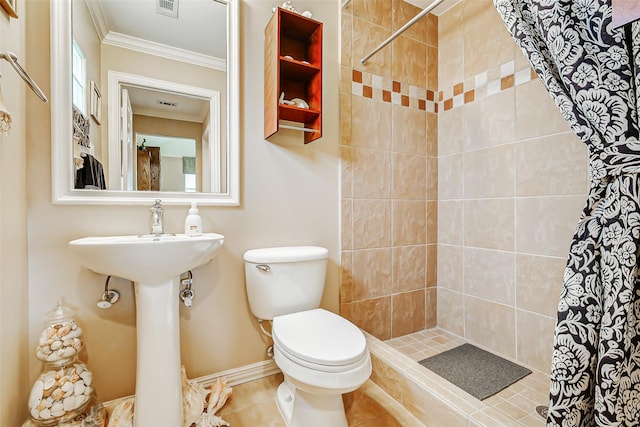 bathroom with crown molding, a tile shower, toilet, baseboards, and visible vents