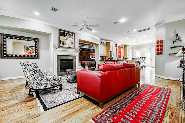 living area with visible vents, ornamental molding, baseboards, ceiling fan, and light wood-type flooring