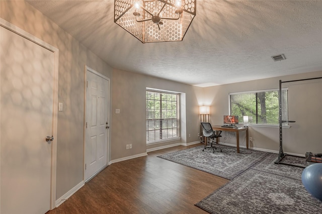 office space featuring an inviting chandelier, a textured ceiling, baseboards, wood finished floors, and visible vents