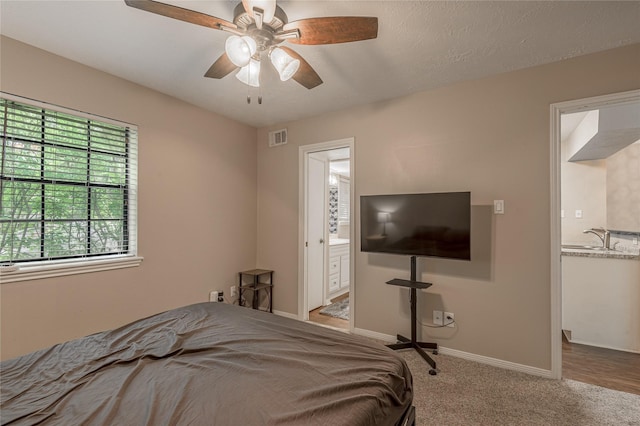 carpeted bedroom featuring ceiling fan, visible vents, a sink, baseboards, and ensuite bathroom