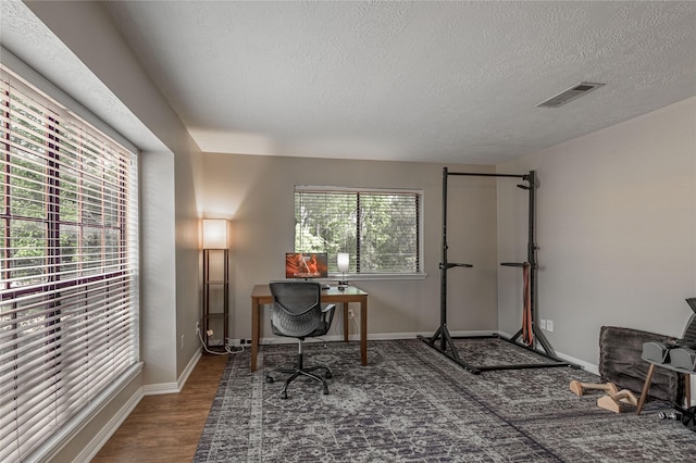 office featuring visible vents, baseboards, a textured ceiling, and wood finished floors