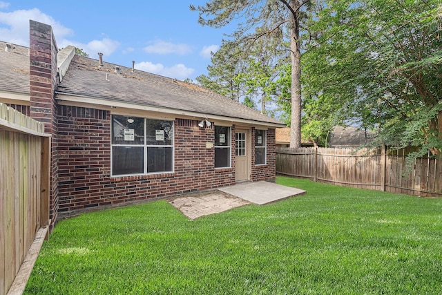 rear view of property featuring a lawn, a fenced backyard, brick siding, and a shingled roof