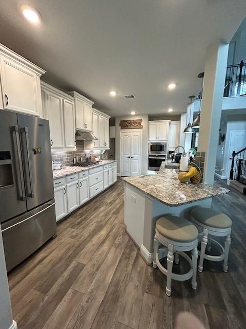 15419 Greenford Glen Dr, Cypress, TX 77429 - kitchen with under cabinet range hood, white cabinetry, stainless steel appliances, and light stone countertops