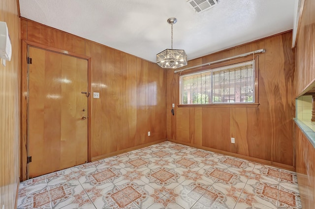 empty room featuring wooden walls, visible vents, an inviting chandelier, and light floors