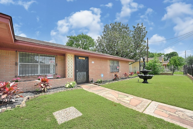 view of front of property featuring brick siding, fence, and a front lawn