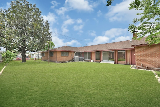 back of house with roof with shingles, brick siding, a chimney, cooling unit, and a lawn