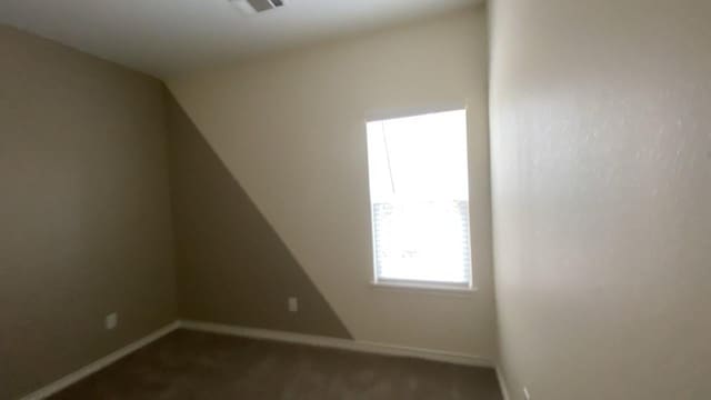 spare room with baseboards, visible vents, and dark colored carpet