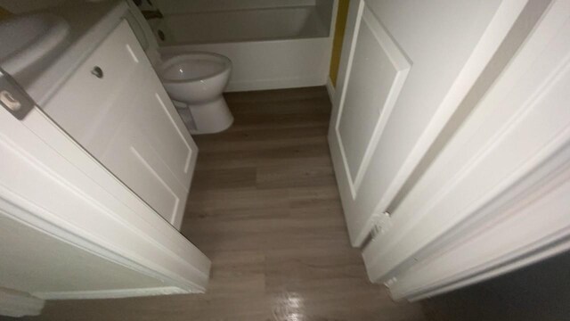 full bath with a bathing tub, toilet, wood finished floors, and vanity
