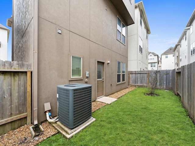 rear view of property featuring a fenced backyard, central AC unit, stucco siding, and a yard