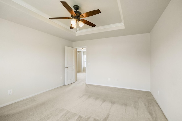 empty room with crown molding, ceiling fan, light carpet, baseboards, and a tray ceiling