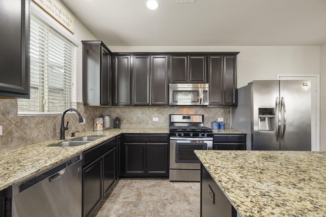 kitchen with light stone counters, a sink, stone finish floor, stainless steel appliances, and decorative backsplash