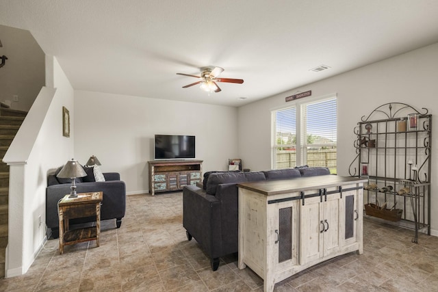 living area with a ceiling fan, baseboards, visible vents, and stairway