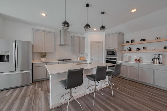 kitchen with gray cabinetry, appliances with stainless steel finishes, a sink, and wall chimney exhaust hood