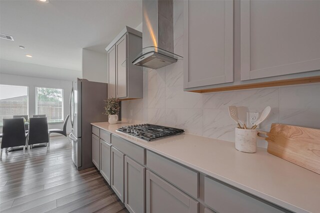 kitchen with gray cabinets, appliances with stainless steel finishes, tasteful backsplash, light countertops, and wall chimney exhaust hood