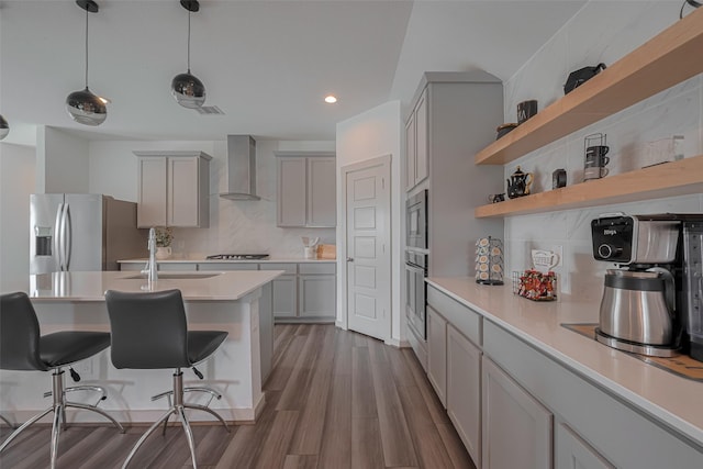 kitchen featuring wall chimney range hood, gray cabinetry, stainless steel appliances, and a sink