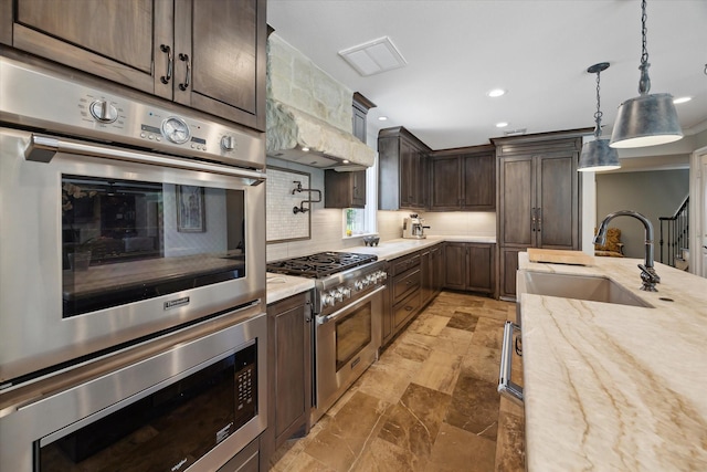 kitchen featuring dark brown cabinetry, light stone countertops, tasteful backsplash, a sink, and stainless steel appliances