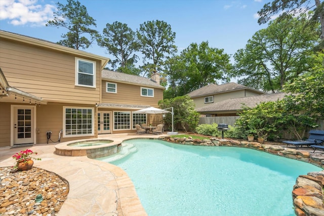 view of swimming pool featuring a patio, a fenced backyard, a pool with connected hot tub, and french doors
