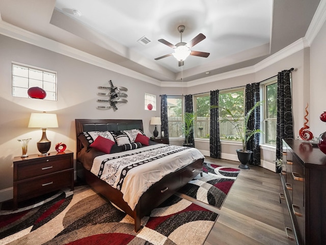 bedroom featuring crown molding, a raised ceiling, wood finished floors, and visible vents