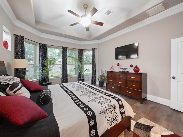 bedroom with visible vents, baseboards, wood finished floors, and a tray ceiling