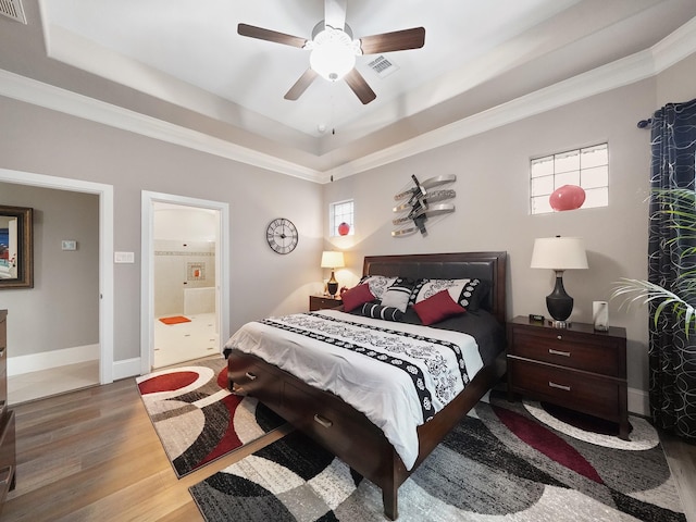 bedroom featuring visible vents, wood finished floors, a tray ceiling, and multiple windows