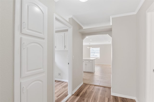 hallway with an inviting chandelier, crown molding, baseboards, arched walkways, and light wood-style flooring