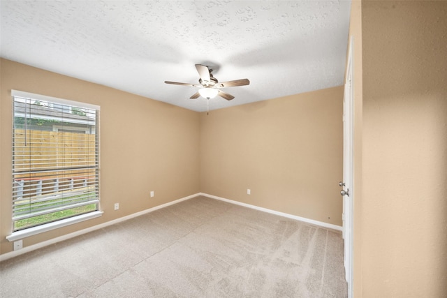 empty room with baseboards, a ceiling fan, a textured ceiling, and light carpet
