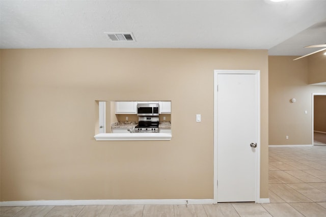 interior space featuring light tile patterned floors, ceiling fan, visible vents, and baseboards