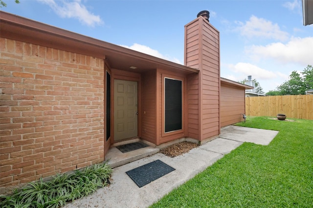 doorway to property with a yard, brick siding, fence, and a chimney