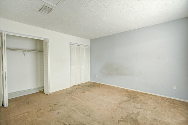 unfurnished bedroom with a textured ceiling, visible vents, carpet floors, baseboards, and two closets