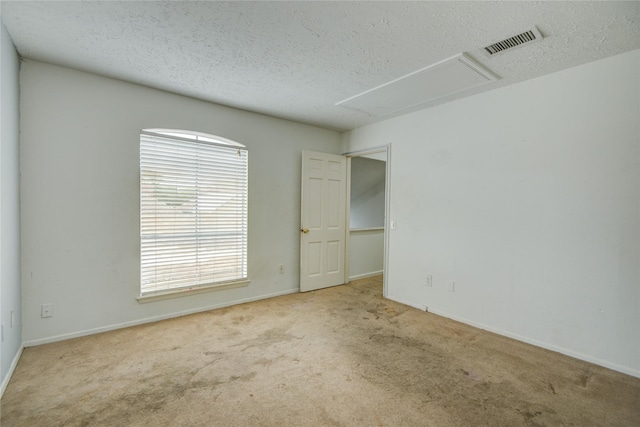 carpeted spare room with a textured ceiling, visible vents, baseboards, and attic access