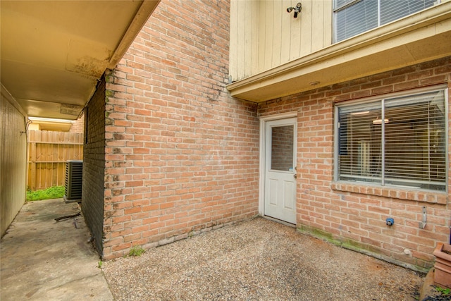 entrance to property with brick siding, cooling unit, fence, and a patio