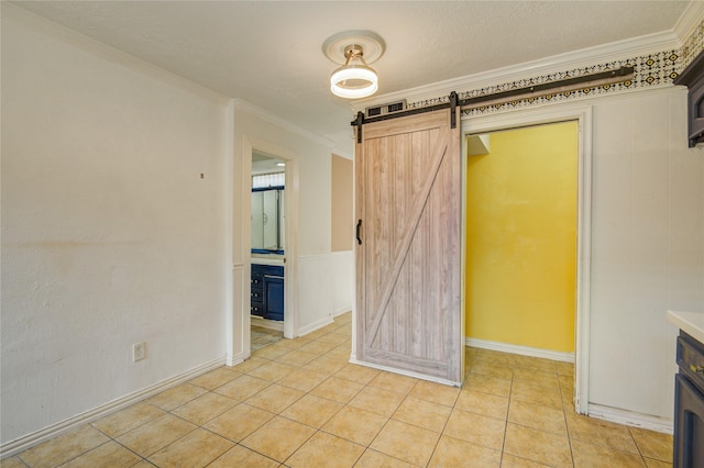 empty room with crown molding, light tile patterned floors, baseboards, and a barn door