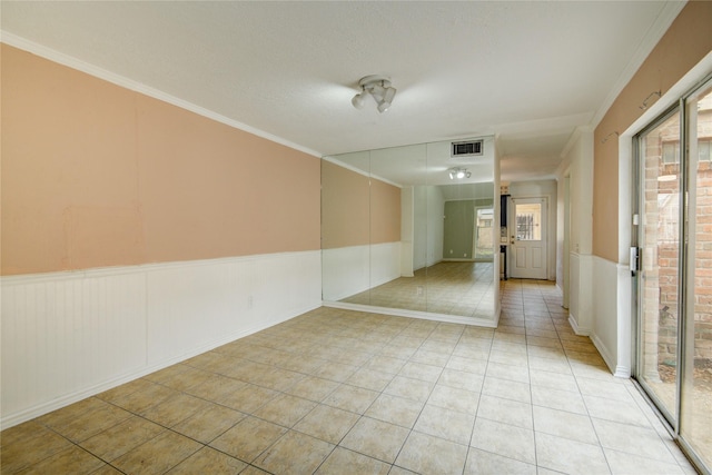 spare room with crown molding, visible vents, wainscoting, and light tile patterned floors