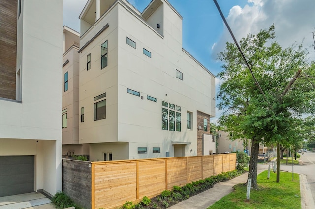 view of side of home with stucco siding, an attached garage, and fence