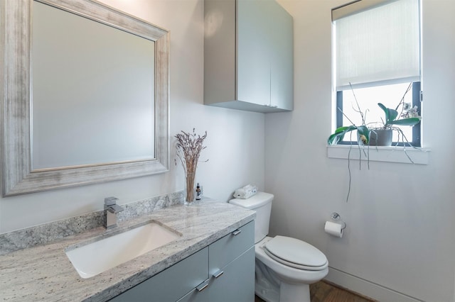 half bathroom with vanity, wood finished floors, and toilet