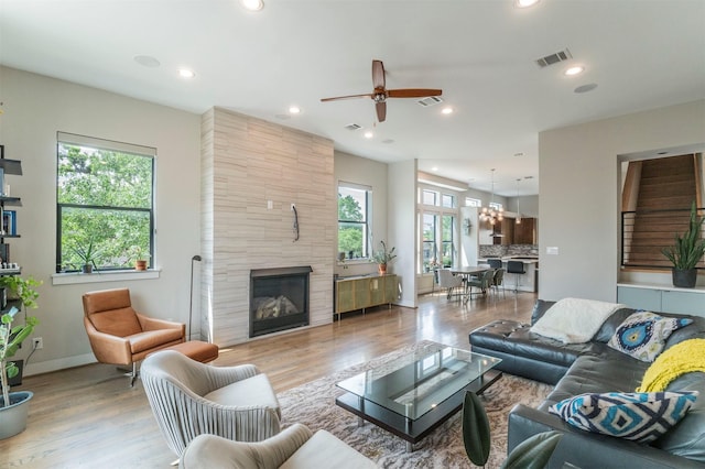 living room with a fireplace, ceiling fan with notable chandelier, wood finished floors, and visible vents