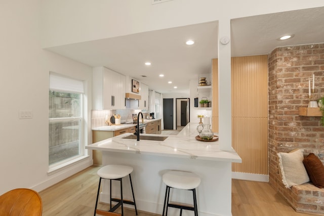 kitchen with a kitchen bar, white cabinetry, light stone counters, a sink, and light wood finished floors
