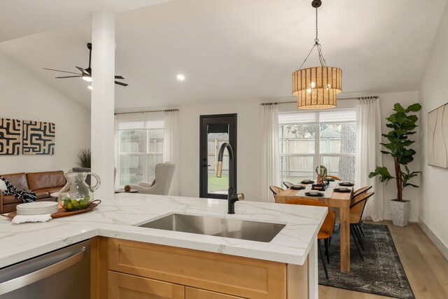 kitchen with a sink, stainless steel dishwasher, light wood-style flooring, and light stone countertops