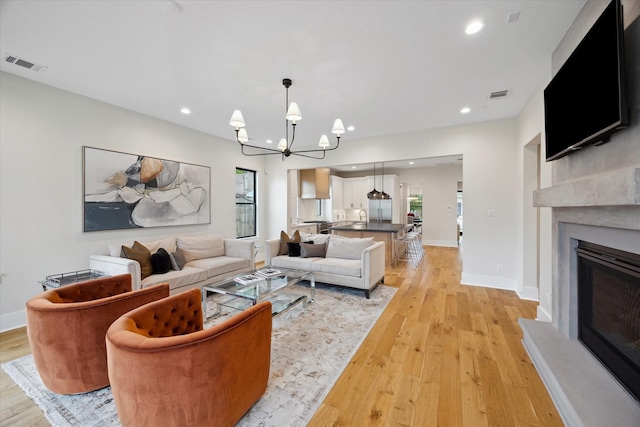 living area with a glass covered fireplace, light wood-style floors, a chandelier, and visible vents