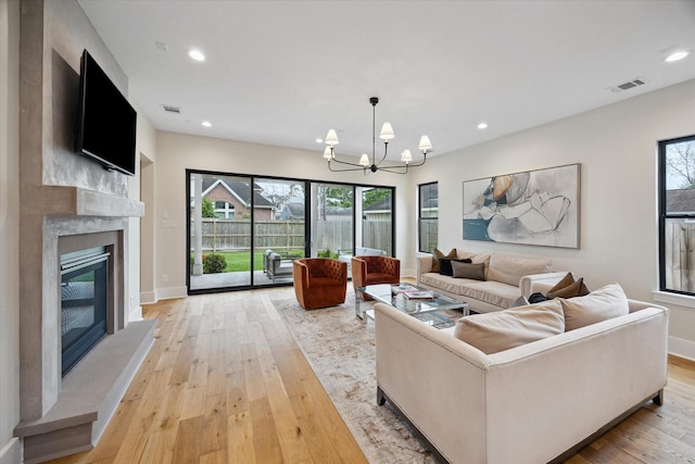 living area with recessed lighting, a notable chandelier, a premium fireplace, and light wood-type flooring