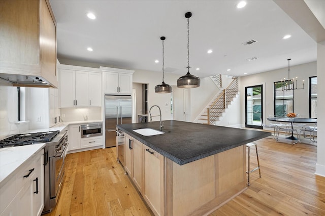 kitchen with a sink, built in appliances, wall chimney exhaust hood, light wood-type flooring, and visible vents