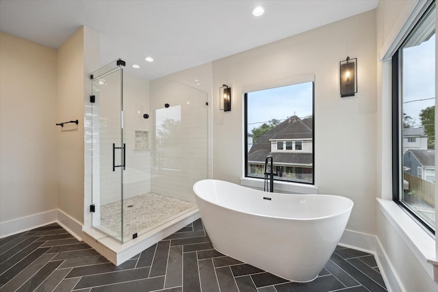 bathroom featuring baseboards, a stall shower, a healthy amount of sunlight, and a soaking tub