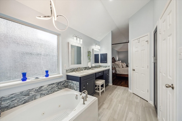 ensuite bathroom featuring connected bathroom, vaulted ceiling, a tub with jets, and vanity