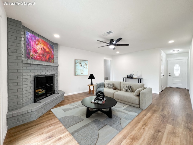 living area featuring a fireplace, a ceiling fan, baseboards, wood finished floors, and visible vents