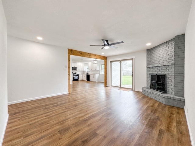 unfurnished living room with a ceiling fan, baseboards, wood finished floors, and a fireplace