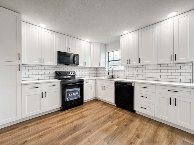 kitchen with a sink, light countertops, a textured ceiling, light wood-style flooring, and black appliances