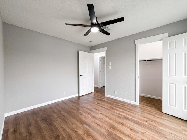unfurnished bedroom featuring a closet, baseboards, light wood-type flooring, a spacious closet, and a ceiling fan