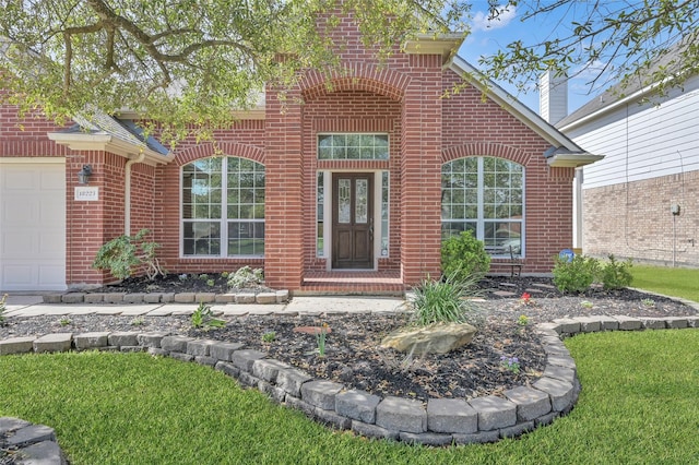view of exterior entry featuring brick siding, an attached garage, and a lawn